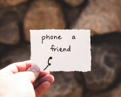 person holding piece of paper with phone a friend written text